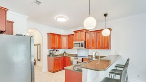 A modern kitchen with wooden cabinets, a stainless steel refrigerator, a microwave, a stove, and a granite countertop. - Charming Navarre Townhome: 5 Mi to Beach! (Navarre)