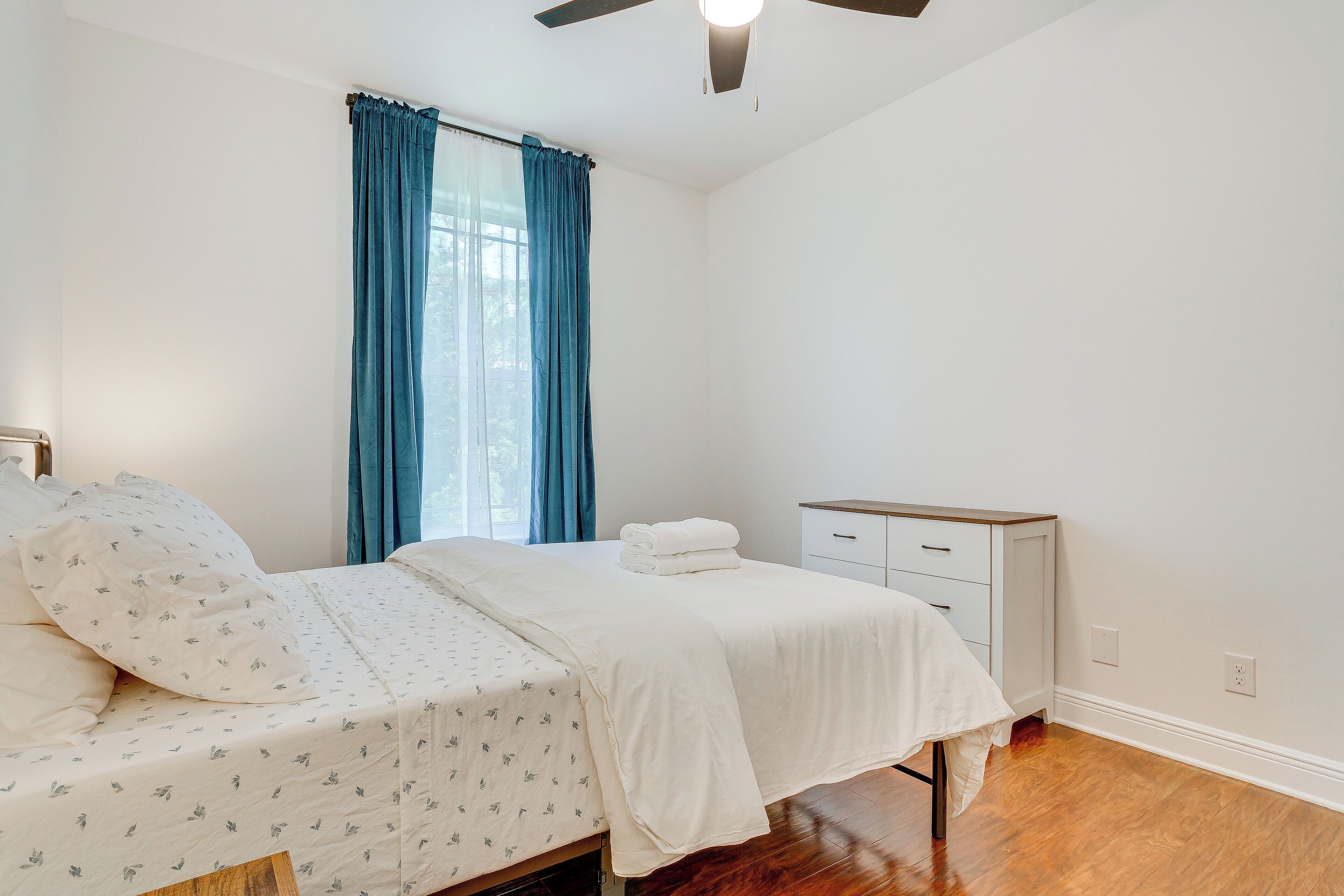 A bedroom with a bed, a nightstand, a dresser, and a window with curtains.