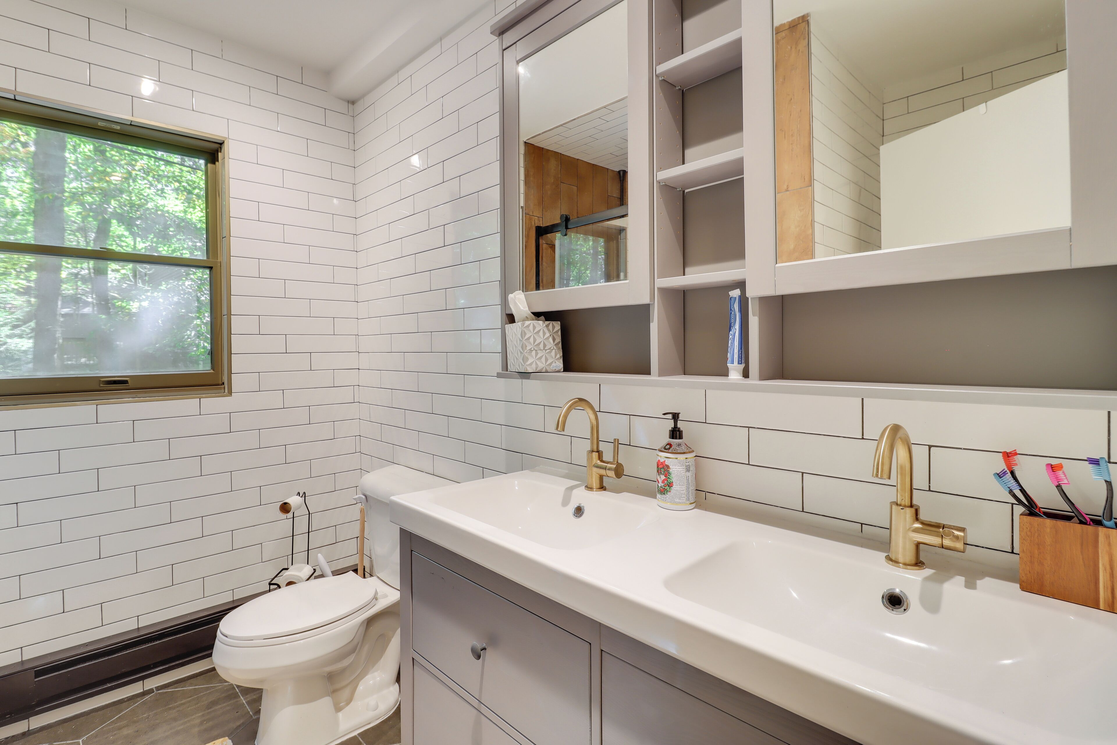 A modern bathroom with white subway tiles, a white sink with gold faucets, and a toilet.