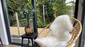 Una silla de mimbre con un cojín blanco mullido en una habitación con un ventanal que da a un espacio exterior.