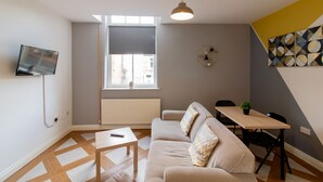 Una sala de estar moderna con un sofá, una mesa de comedor y un televisor montado en la pared.