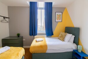 A bedroom with a bed, a bedside table, a small nightstand, a window with curtains, and a wall art piece. - Stunning 1-bed Apartment in Gateshead (Gateshead)