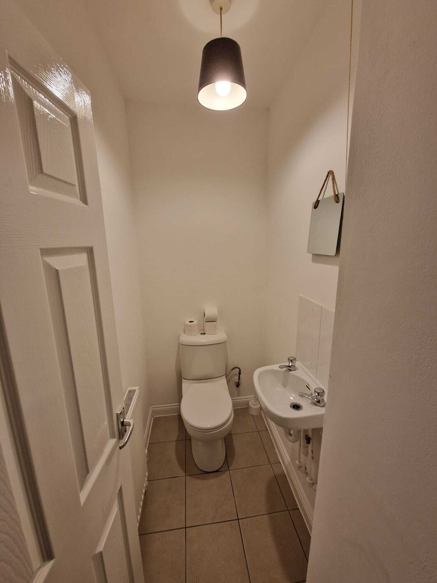 A small, narrow bathroom with a toilet, sink, and a hanging light fixture.