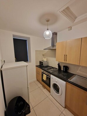 A compact kitchen with a washing machine, microwave, stove, and wooden cabinets.