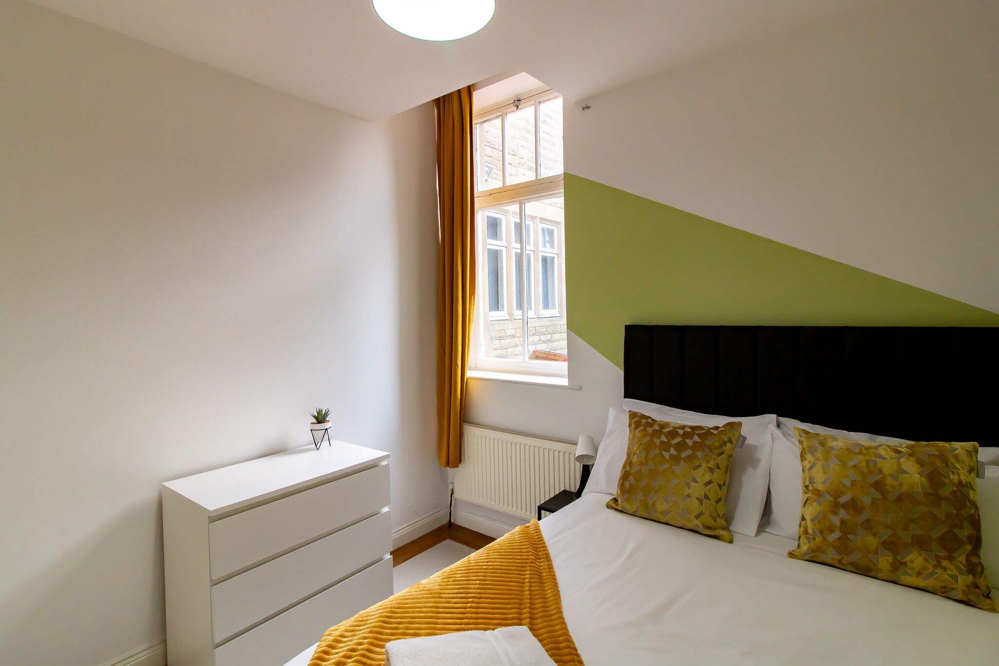A modern bedroom with a bed, bedside table, and a window with curtains.