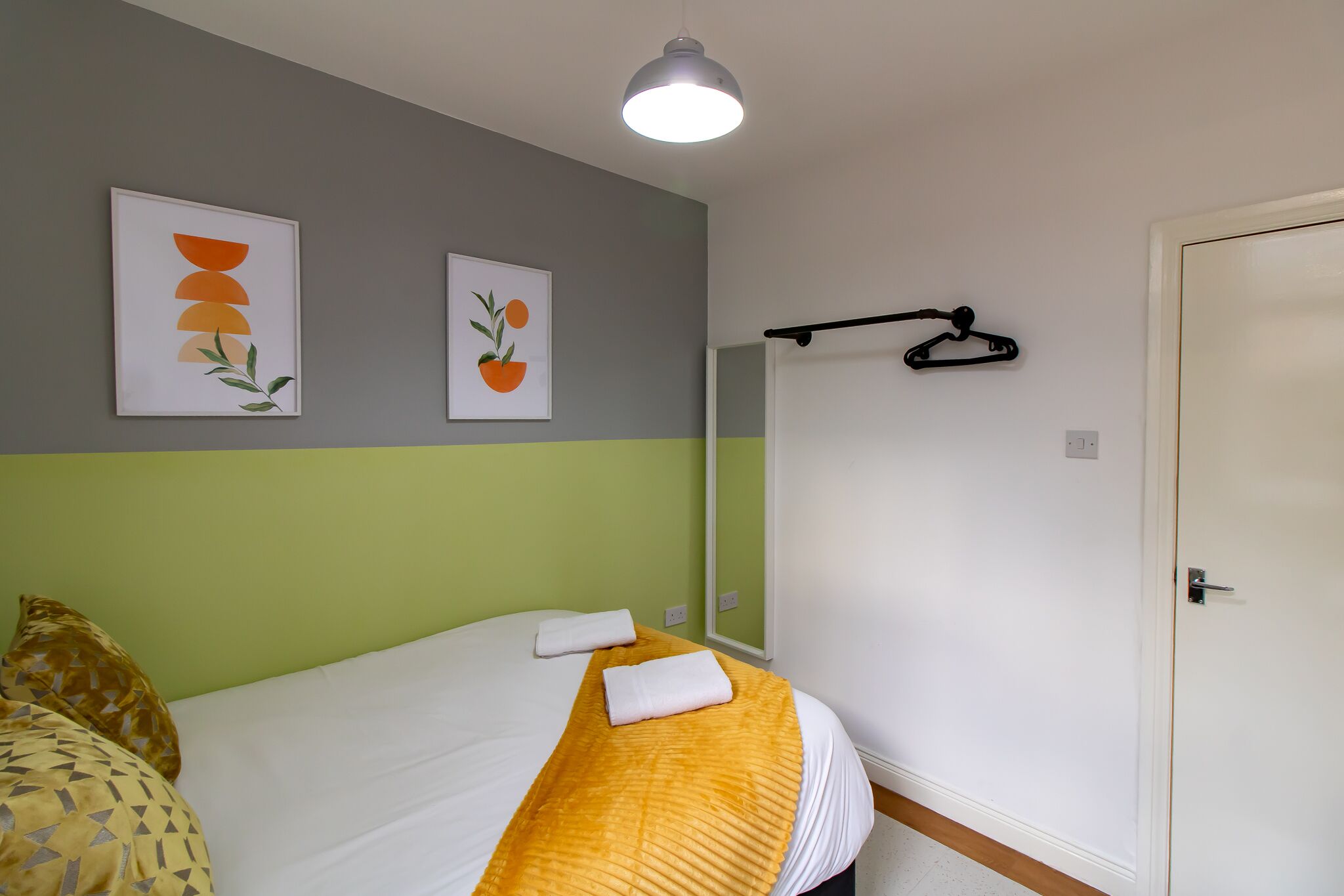 Une chambre d’hôtel avec un lit, un porte-manteau mural et deux œuvres d’art encadrées accrochées au mur.