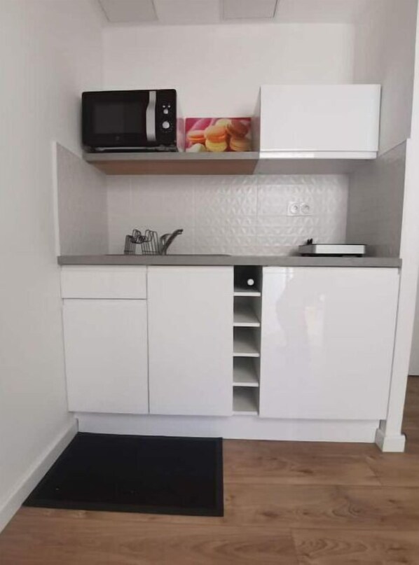 Compact kitchen with sink, microwave, and shelf.