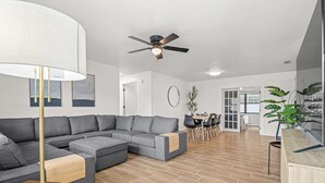 Un salon moderne avec un canapé d’angle, un coin repas comprenant une table et des chaises, et un ventilateur de plafond.