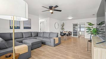 A modern living room with a sectional sofa, a dining area with a table and chairs, and a ceiling fan.