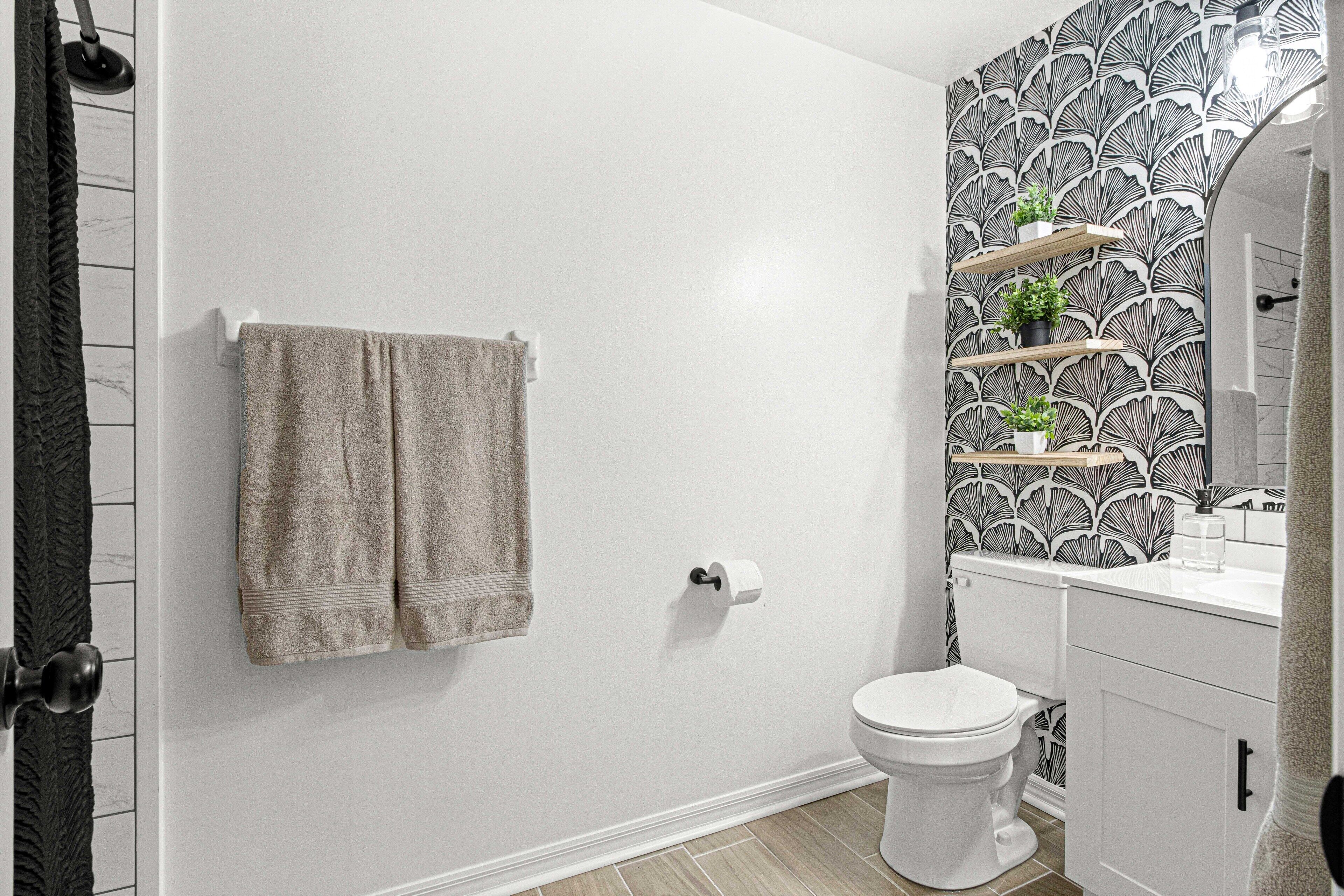 Un baño con inodoro blanco, dos toallas colgadas en la pared y un papel tapiz estampado.