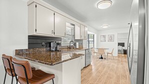 Une cuisine moderne dotée d’un plan de travail en granit, d’appareils électroménagers en acier inoxydable et d’un coin repas avec une table et des chaises.