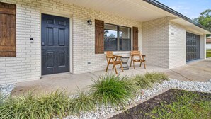 Une maison avec une façade en briques blanches, une porte d’entrée noire et un porche couvert avec des chaises et une table en bois.