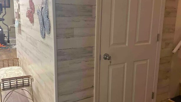 Een kamer met een witte deur, een houten vloer en een muur met decoratieve vlinder- en bloemkunst.