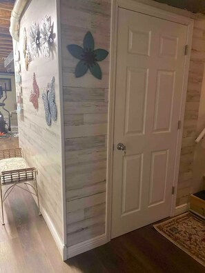 A room with a white door, a wooden floor, and a wall with decorative butterfly and flower art.