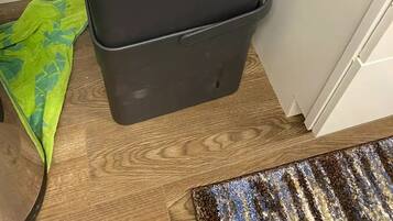Un termosifone portatile nero con un pannello di controllo e un cavo di alimentazione, posizionato su un pavimento in legno accanto a un asciugamano verde e un tappeto decorato.