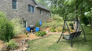 Een stenen huis met een schommel in de tuin, een barbecue en een tuin met verschillende planten.