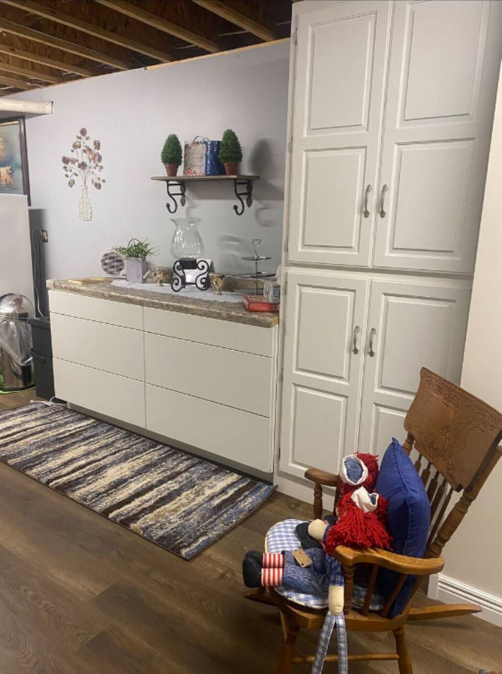 A compact kitchen with white cabinets, a wooden chair with a cushion, and a small rug on the floor.
