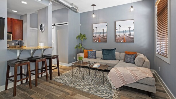 A modern living room with a sofa, coffee table, and bar stools. There is a kitchen area with a countertop and cabinets. - Downtown Chattanooga Loft in the Heart of the City (Chattanooga)