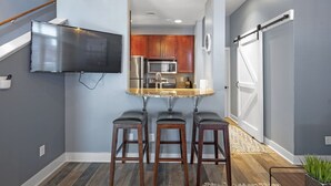 A modern kitchen with a central island, wooden stools, and a flat-screen TV mounted on the wall. - Downtown Chattanooga Loft in the Heart of the City (Chattanooga)