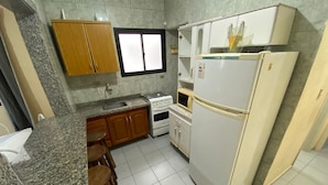 Eine kompakte Küche mit Granit-Arbeitsplatten, Holzschränken, einem weißen Kühlschrank, einer Mikrowelle und einem Herd.