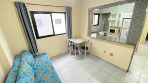 Ein Zimmer mit einem Bett, einem kleinen Tisch mit Stühlen, einer Küchenzeile mit einer Mikrowelle und einem Fenster mit Vorhängen.