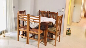 Un coin repas avec une table et des chaises en bois, un rideau blanc et un sol carrelé.