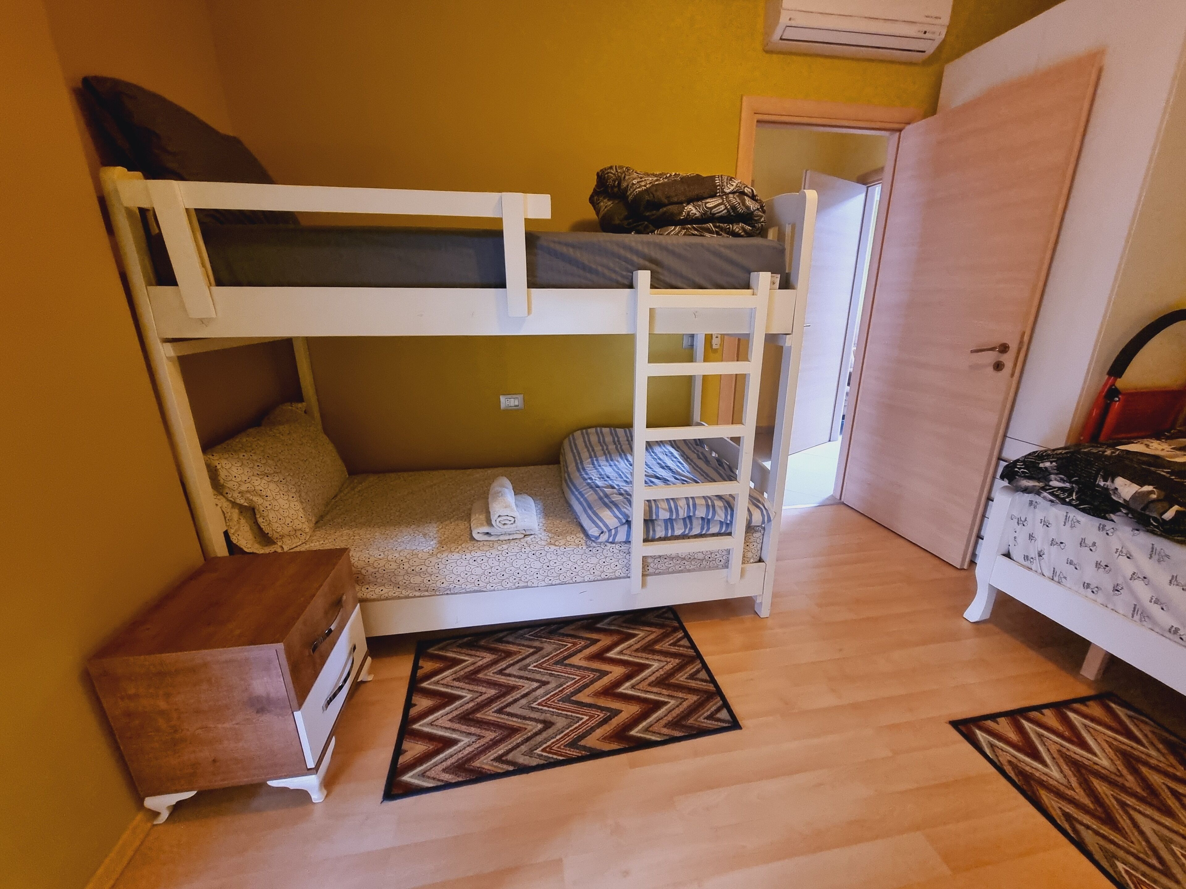 A bunk bed room with a wooden dresser, a door, and a patterned rug.