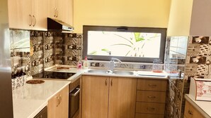 Une cuisine de taille réduite, dotée de meubles en bois, d’un évier en acier inoxydable et d’un dosseret carrelé.