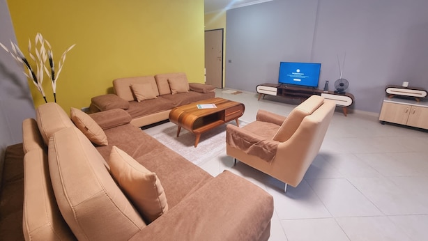 Un salon moderne avec un canapé d’angle, une table basse et un téléviseur en arrière-plan.