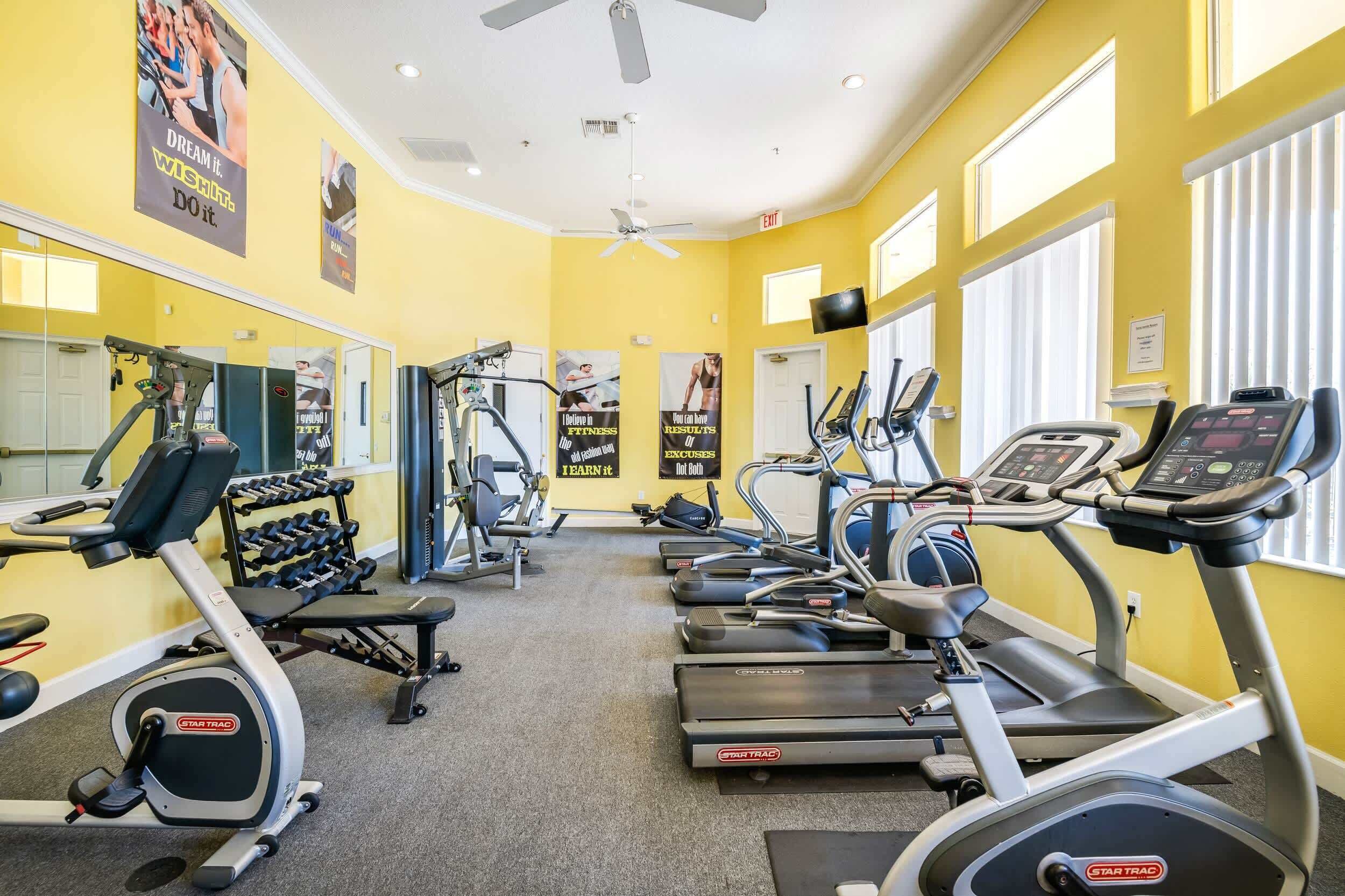 A gym with various cardio machines, weightlifting equipment, and motivational posters on the walls.