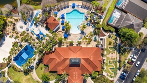 Una vista aerea di un resort con piscina centrale, campo da tennis e area patio coperta.