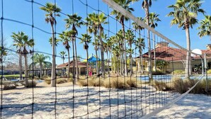 Una spiaggia con una rete da pallavolo, palme e un edificio con tetto rosso sullo sfondo.