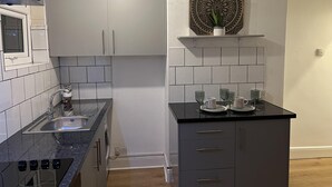 A compact kitchen with white cabinets, a black countertop, and a decorative wall piece. - Apartment in Leicester- Doublebed-citycentre-wifi (Leicester)