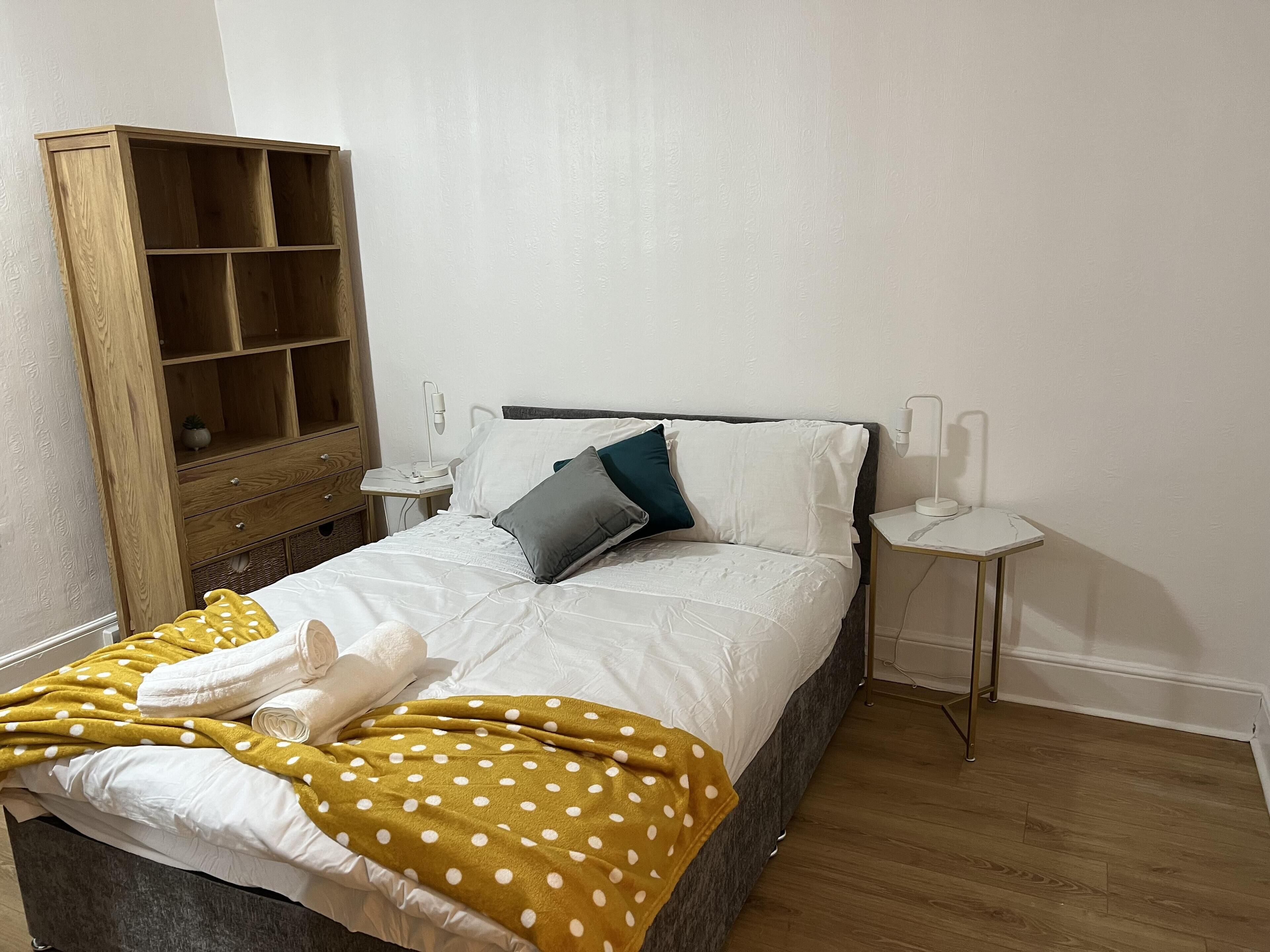 Un letto rifatto con coperte bianche e gialle a pois, un armadio in legno e due lampade da comodino.