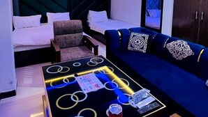 A modern hotel room with a dark blue sofa, a black coffee table with circular light accents, a ceiling fan, and a large window with curtains. - Hotel 11 (Islamabad)