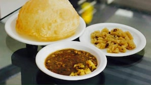 A table with a plate of food, including a bread-like item, a bowl of curry, and a plate of what appears to be a vegetable dish. - Hotel 11 (Islamabad)