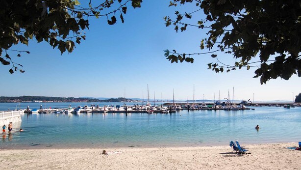 Un port de plaisance avec des bateaux amarrés, une plage de sable et un ciel bleu dégagé.