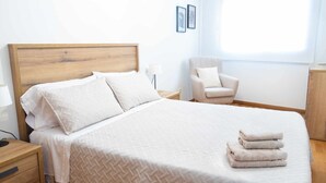 Un lit bien fait, avec une tête de lit en bois, une chaise et une pile de serviettes.