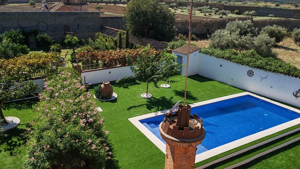 A swimming pool with a brick tower, surrounded by a well-maintained garden with various plants and a view of distant hills.