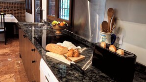 A kitchen with a granite countertop, a bread loaf, a cutting board, a knife, a toaster, and a bowl of fruit.