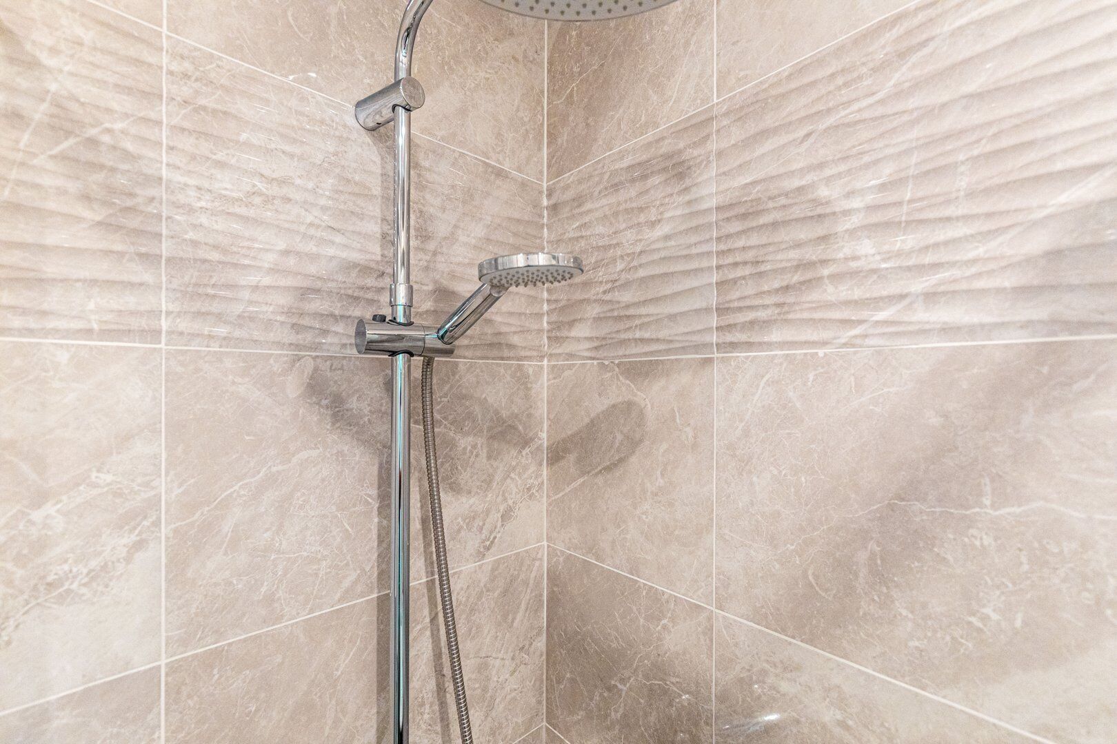 Une douche équipée d’un pommeau de douche à main et d’un pommeau de douche fixe fixé au mur, tous deux dotés de finitions chromées.