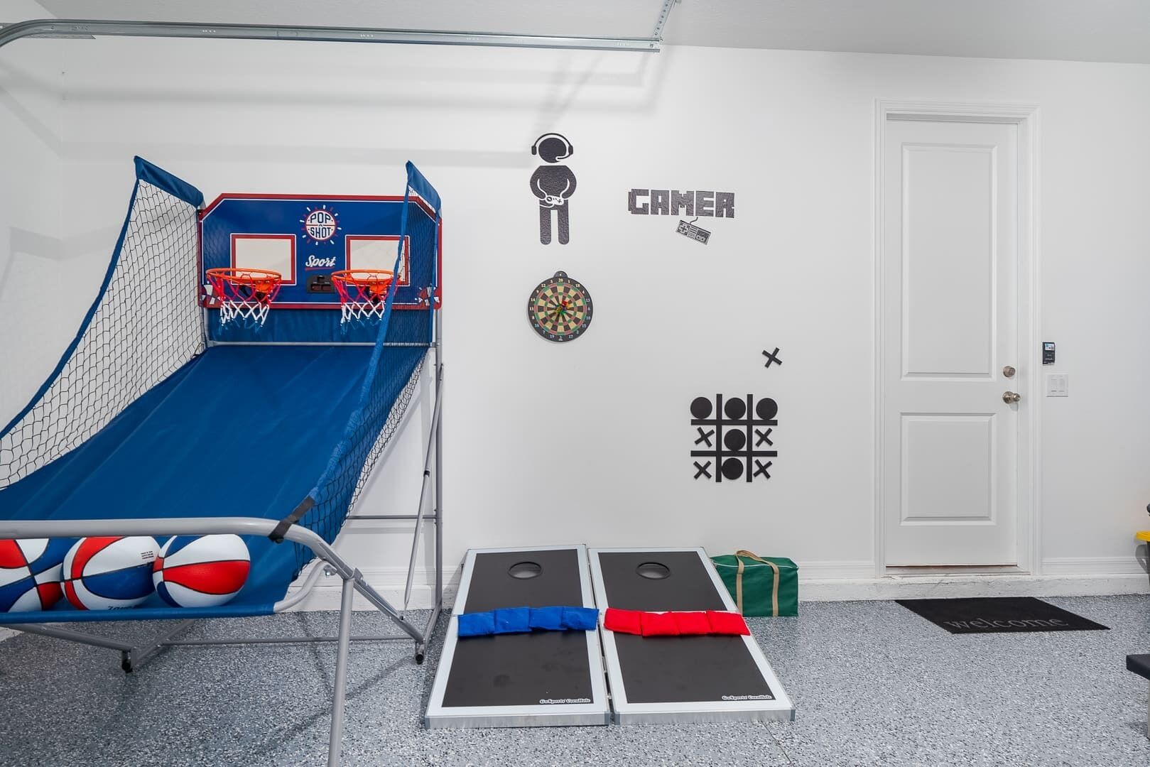 Een kamer met een blauwe basketbalring, dartbord, een tic-tac-toe spel en een welkomstmat.