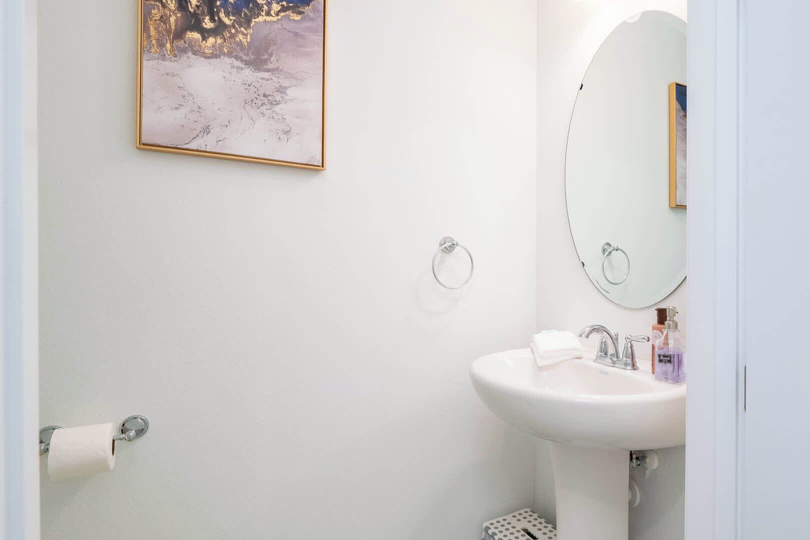 A bathroom with a white sink, a mirror, a toilet paper holder, and a towel rack.