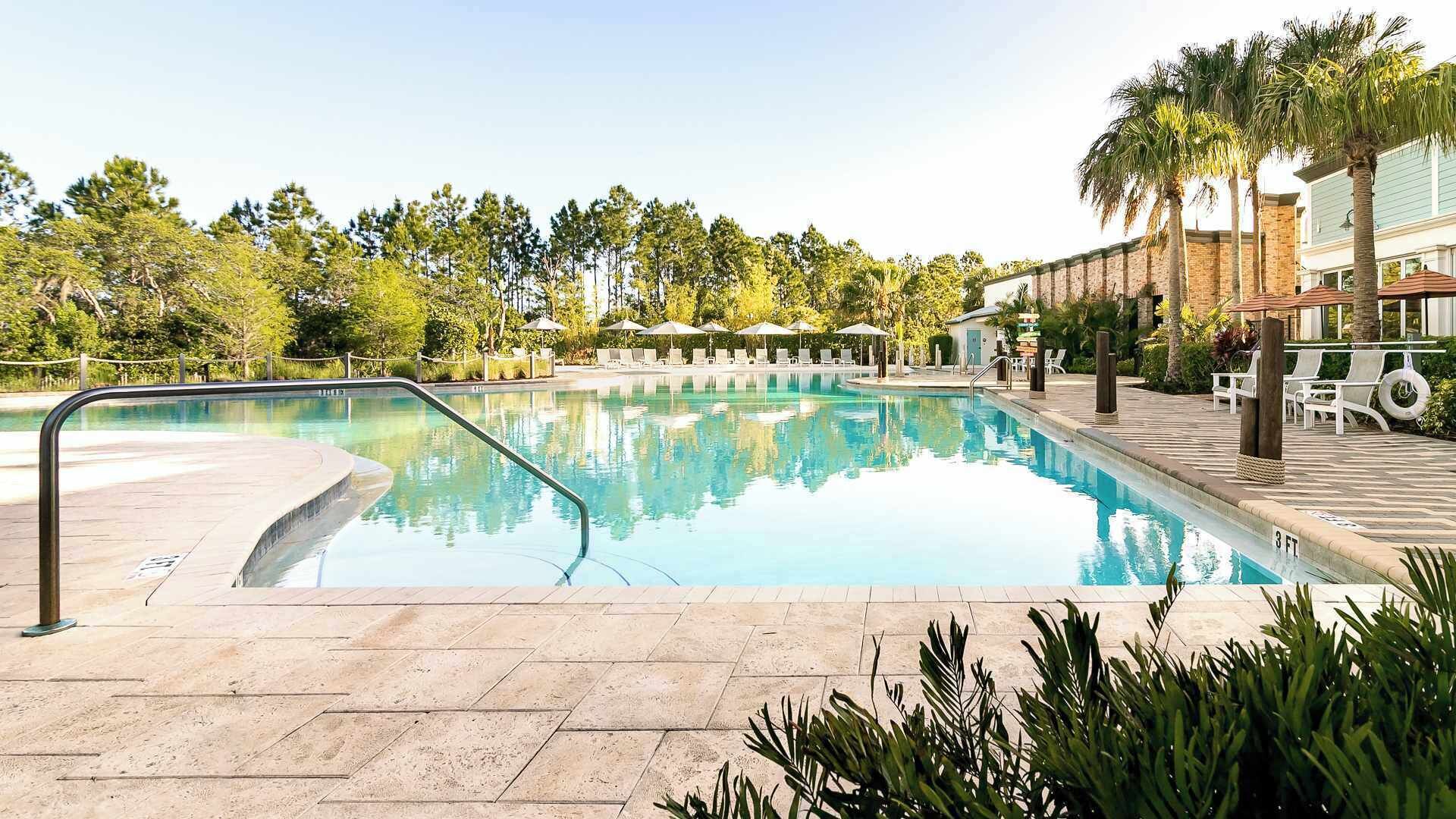 A swimming pool with lounge chairs and umbrellas, surrounded by trees and a building.