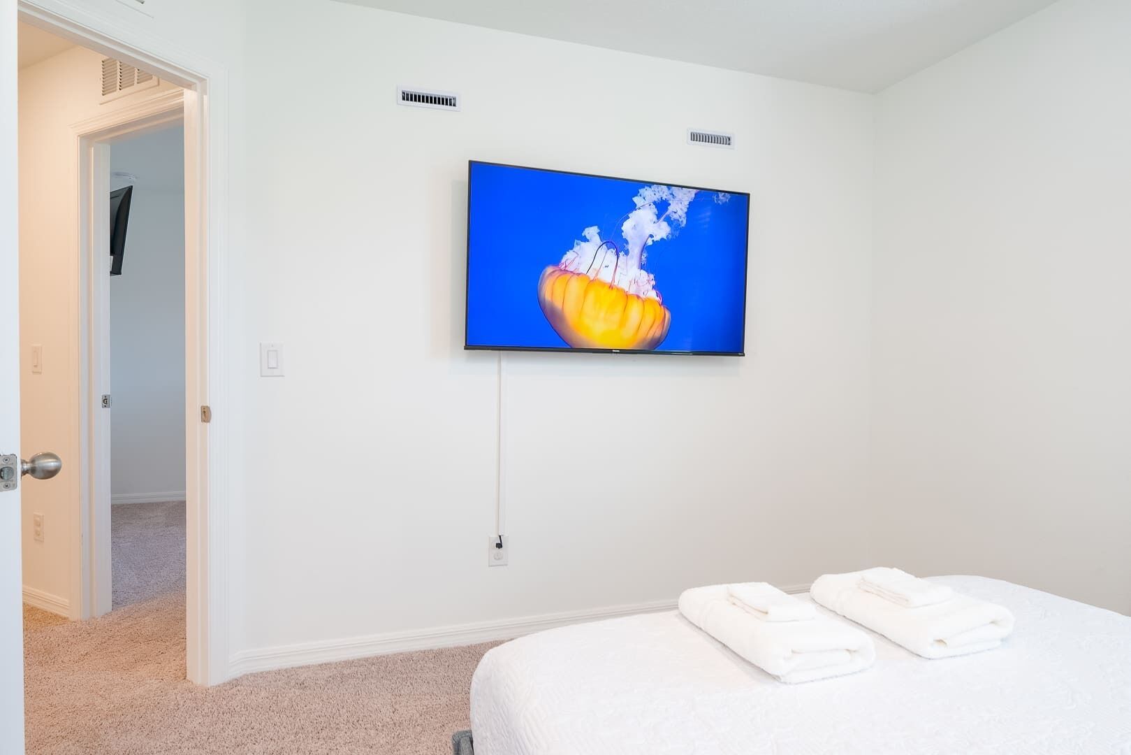 A hotel room with a bed, a television mounted on the wall, and a door leading to another room.