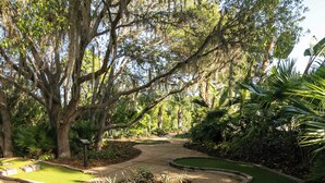 Um caminho serpenteia por um jardim com árvores frondosas e um pequeno lago.