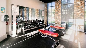 Uma academia com equipamentos de ginástica, um banco de musculação e uma parede com padrão de tijolos.