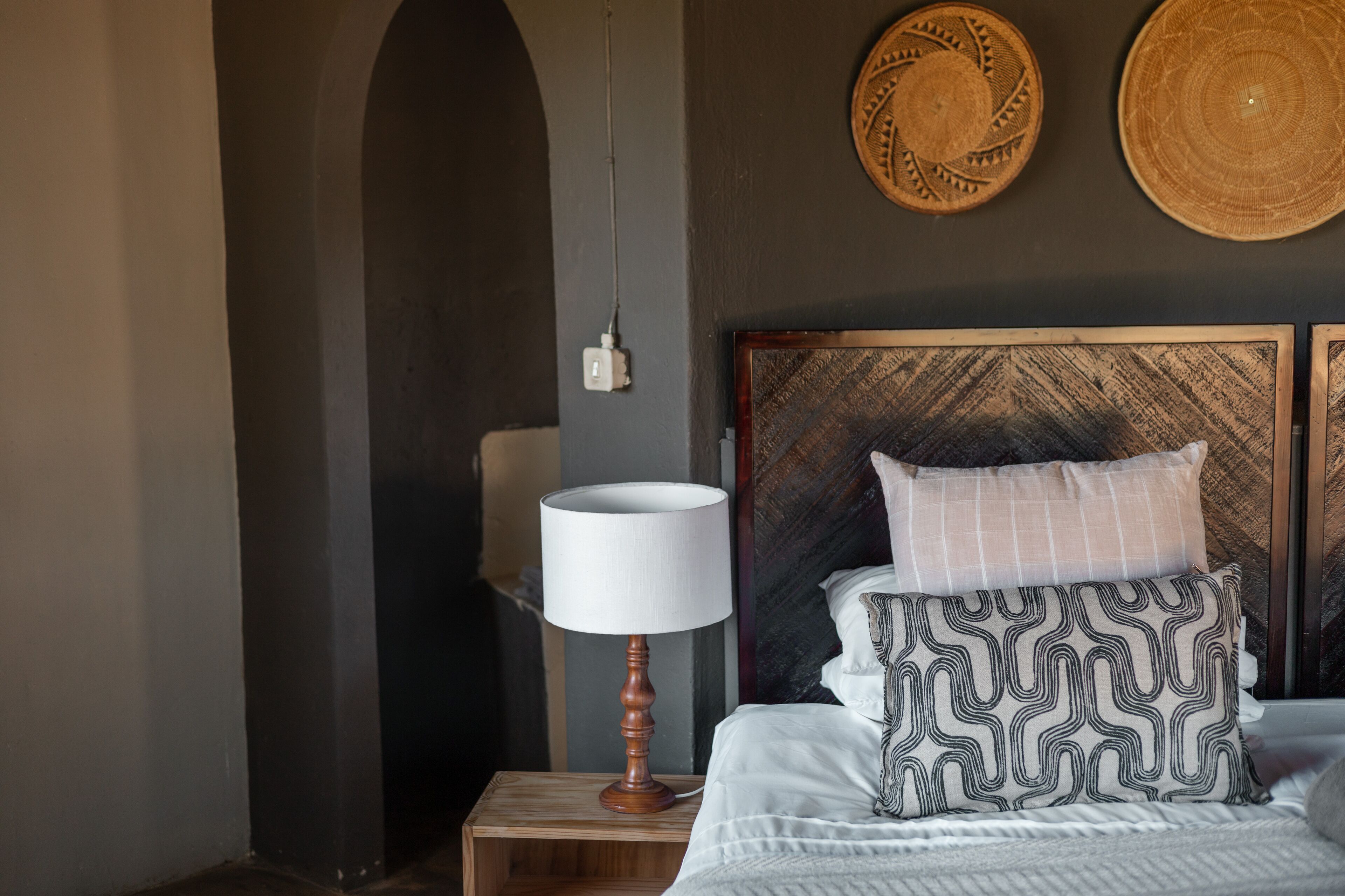 A neatly made bed with patterned pillows, a bedside lamp, and two woven wall hangings.