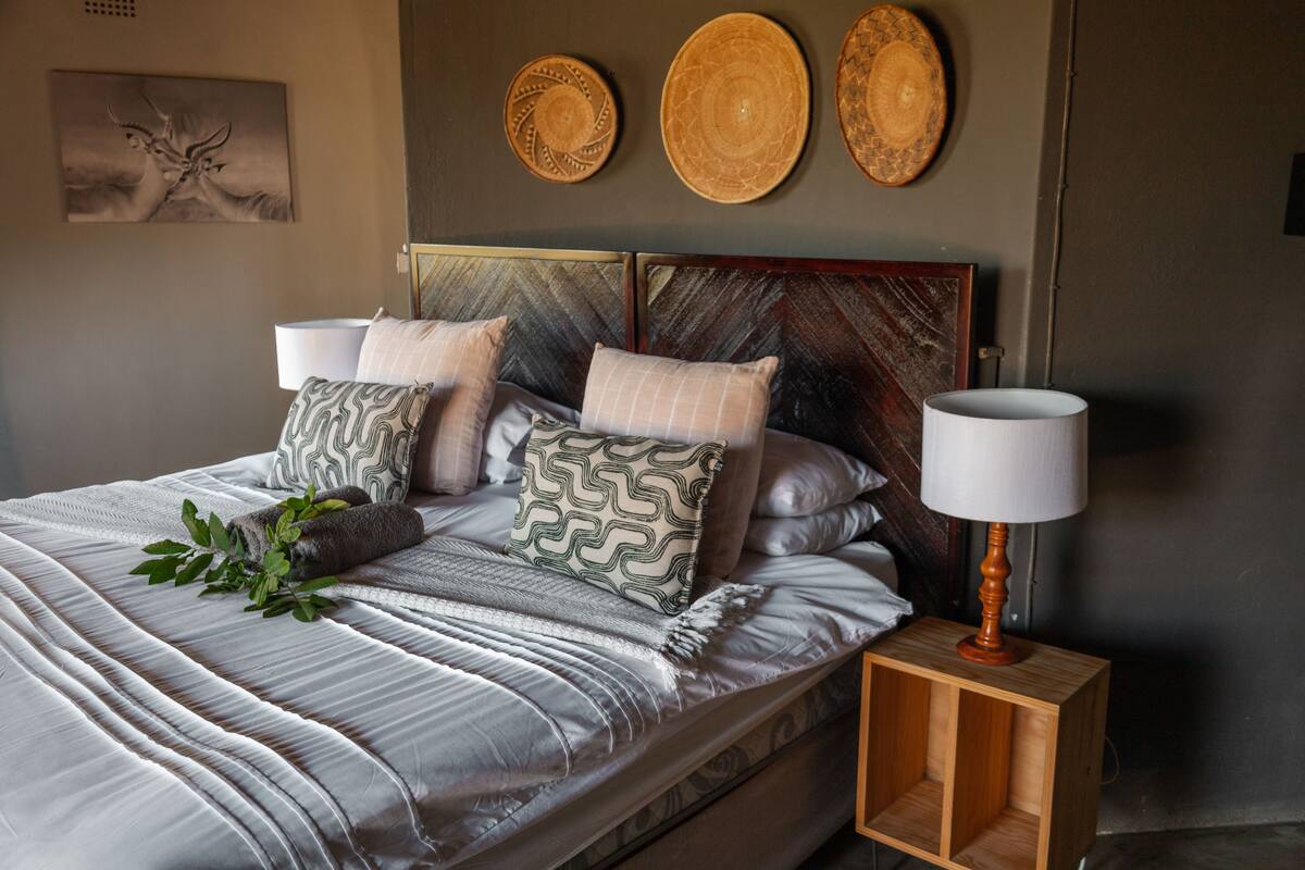 A neatly made bed with a striped bedspread and multiple pillows, a bedside table with a lamp, and three decorative plates on the wall.