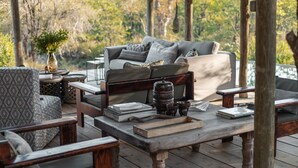 A wooden deck with a sofa and chairs, books, and a decorative vase. - Nsala Wilderness Camp (Hoedspruit)